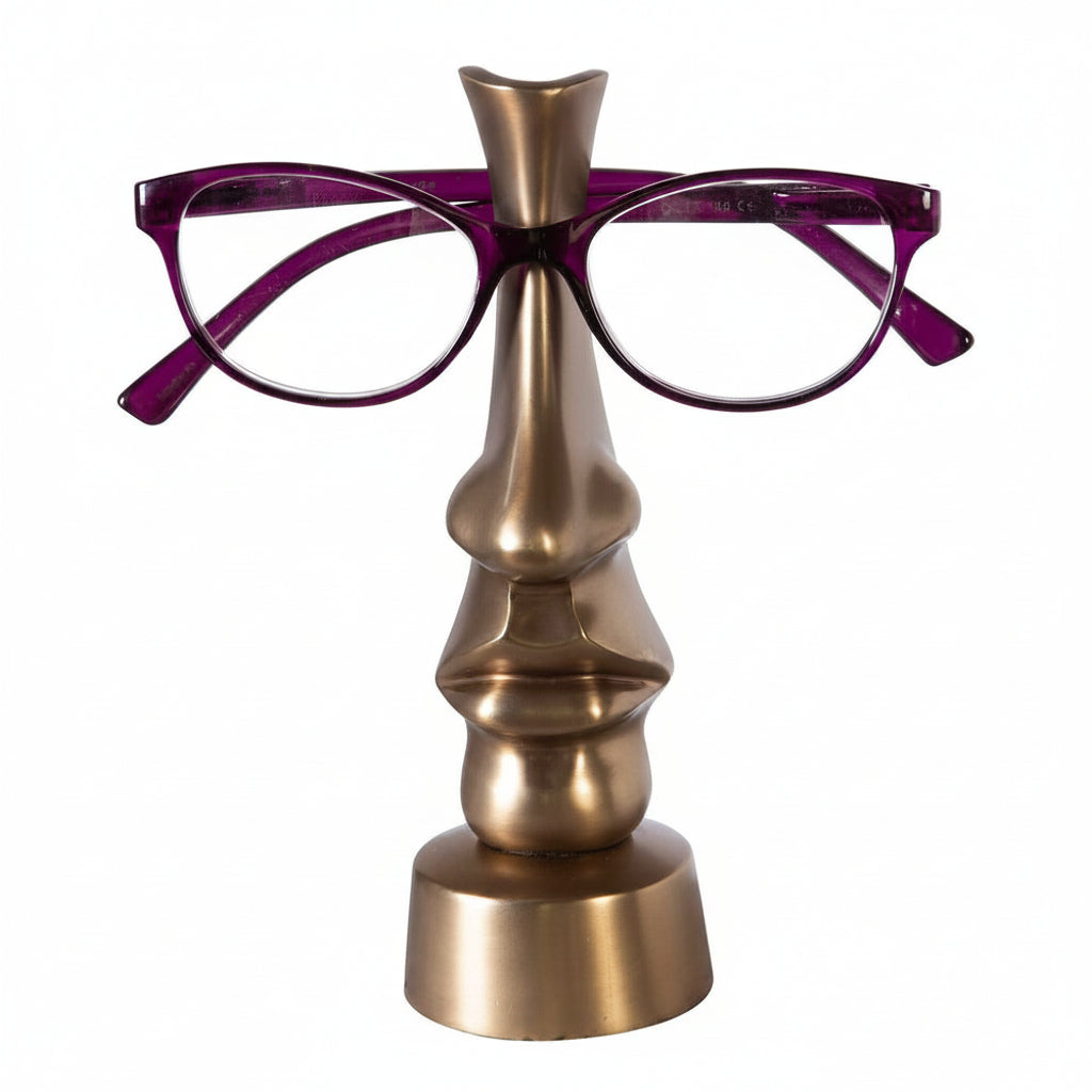 A bronze-colored metal glasses holder in the shape of a stylized female face, with a pair of purple eyeglasses placed on it.