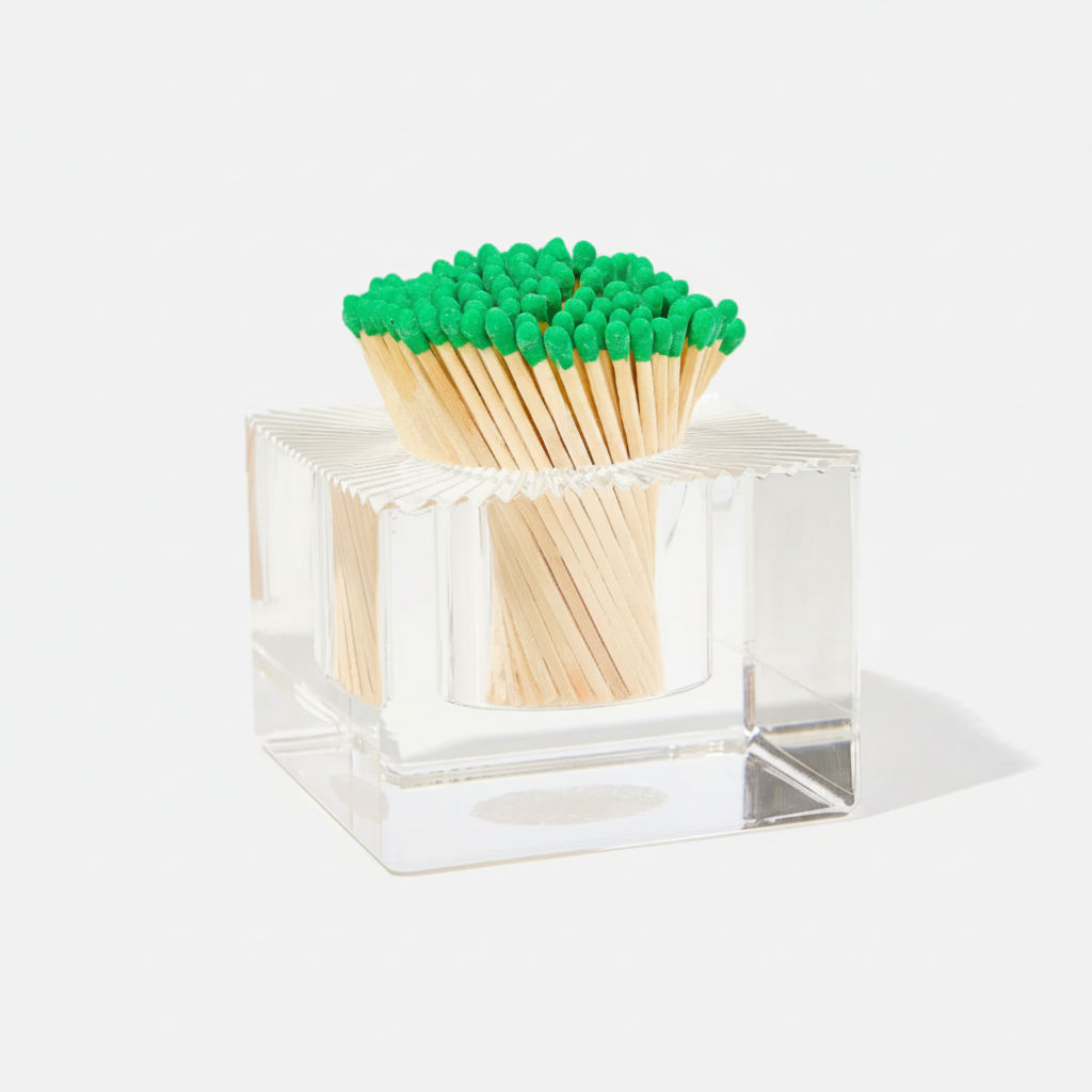 Clear cube-shaped matchbox with green matches on a white background